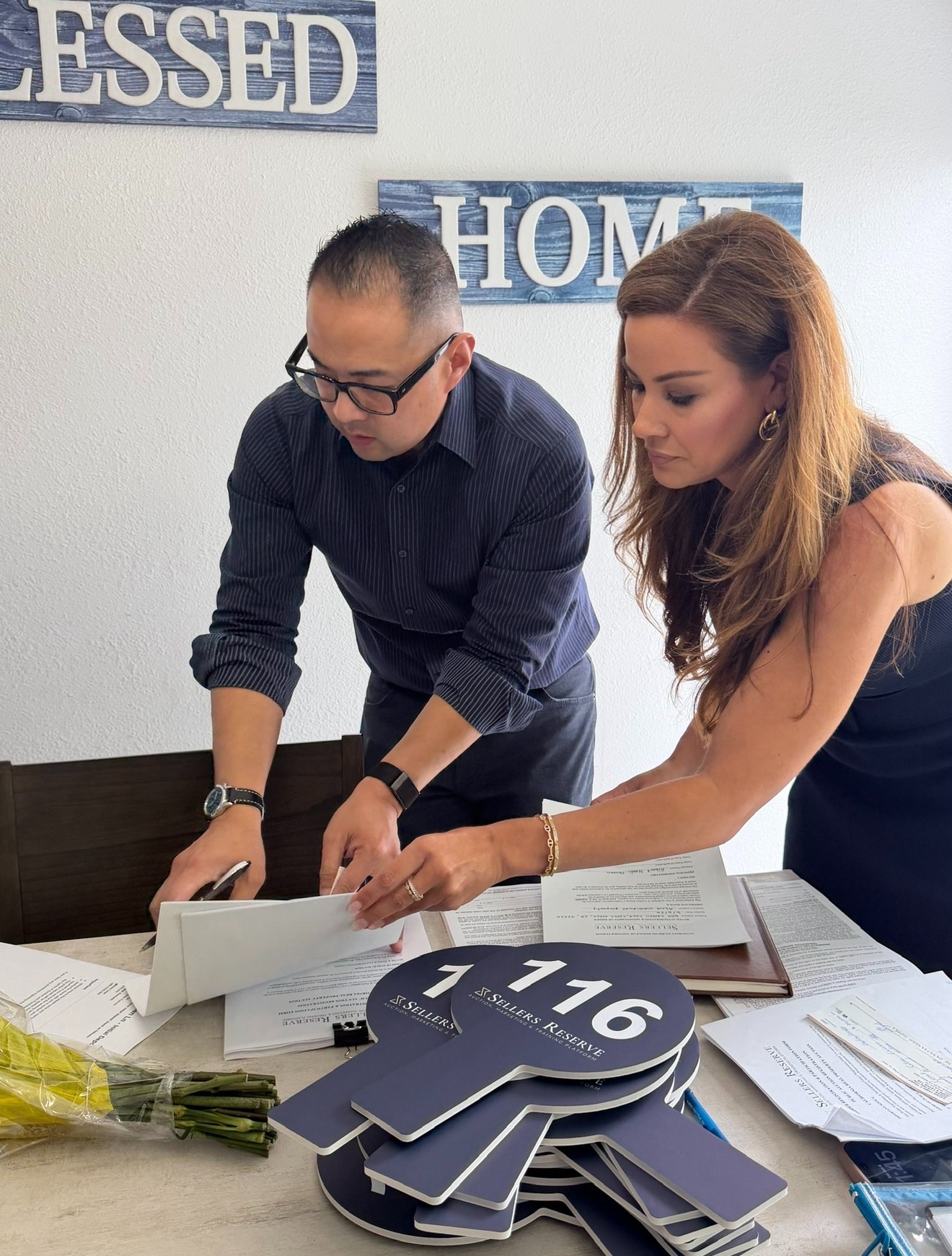 Two agents reviewing Sellers Reserve auction paperwork and bidder paddles at a listing appointment